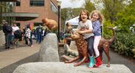 Two girls sit on a bronze golden retriever statue in front of Magruder Hall